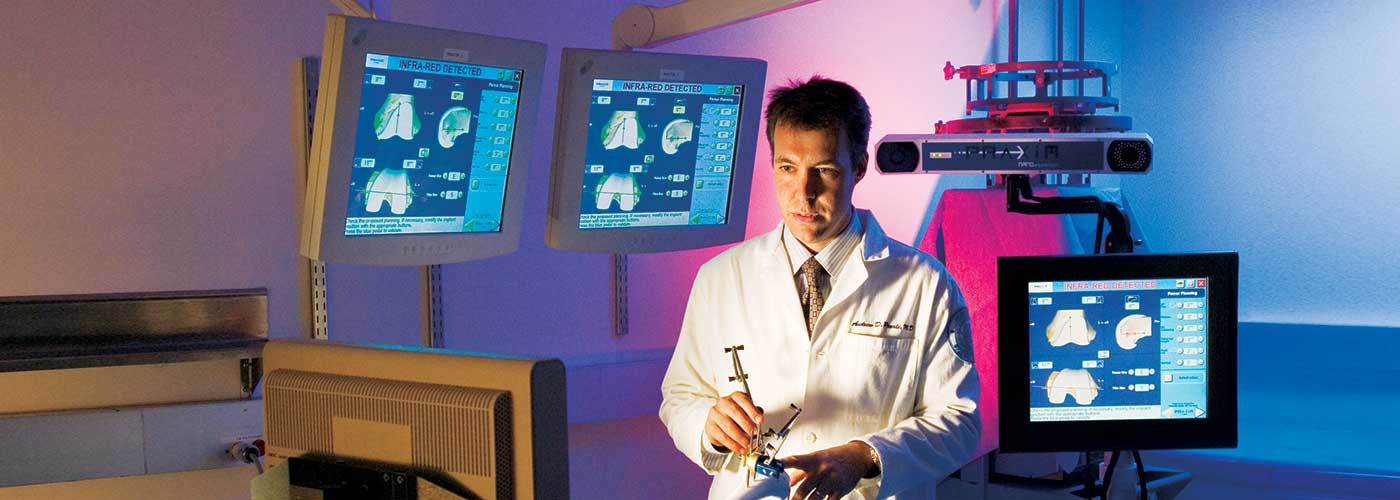 Banner image of Dr. Andrew Pearle demonstrating computer assisted surgery.