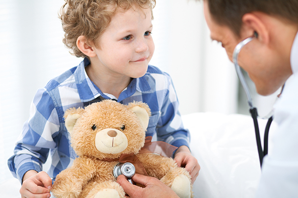 photo of child holding bear being examined by doctor