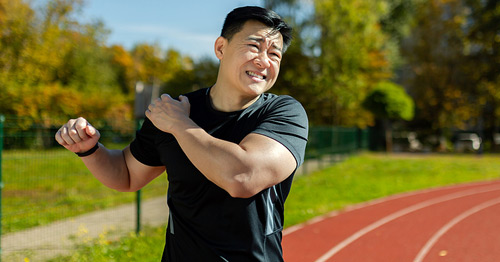 An active man on a running track experiencing shoulder pain.