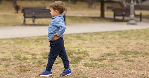 A little boy walking, holding his hip.