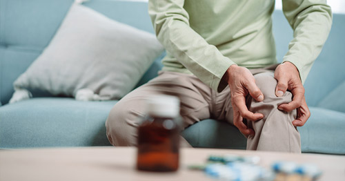 A man holding his knee in pain near a bottle of pills.