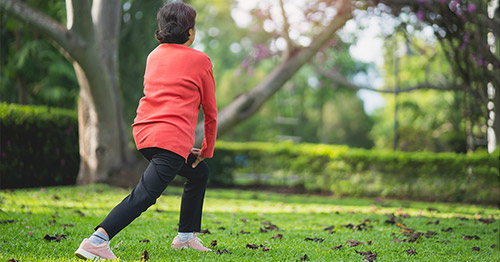 An older woman doing knee bends outside.