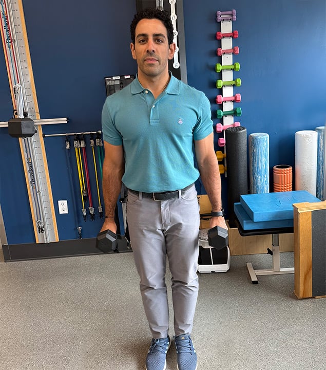 Man standing holding weights at his side with arms relaxed.