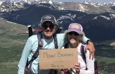 Man and woman at summit of mountain displaying cardboard sign that says Mount Bierstadt