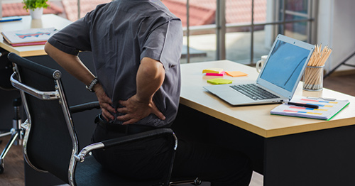 A man at an office desck holding his lower back in pain.