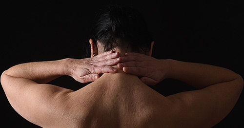 A middle aged woman holding her neck in pain.