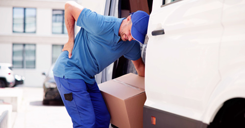 A man bending and twisting while lifting a box, with a facial expression suggesting he is in pain.