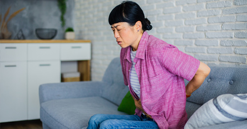 A woman sitting holding her lower back in pain.