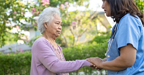 An older woman with a female doctor in a garden setting.