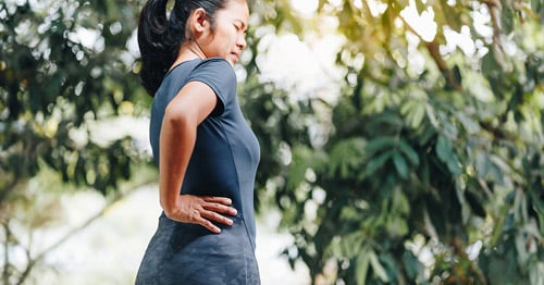 A woman grabbing her lower back and hip in pain.