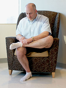 Photo of a man crossing his ankle over his knee to put on his sock.