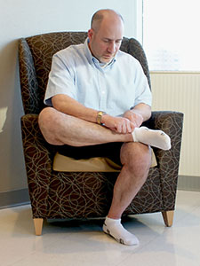 Photo of a man crossing his ankle over his knee to put on his sock.