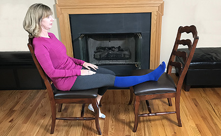 Photo of a woman sitting in a chair correctly with her right leg elevated and resting on a second chair