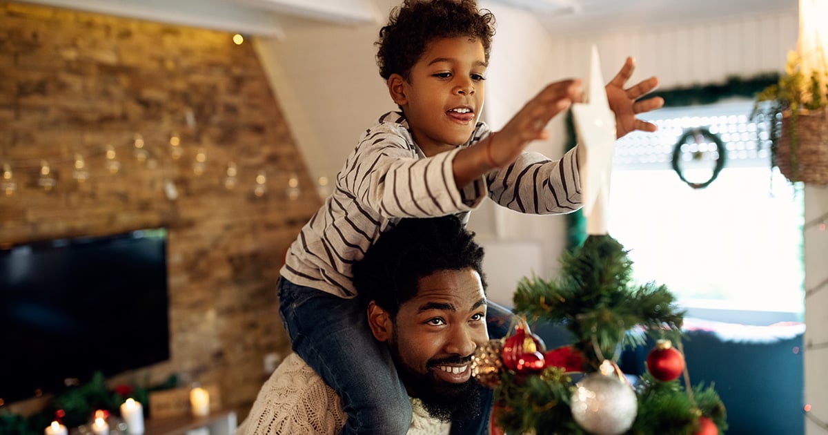 Man with child on his shoulders decorating a holiday tree
