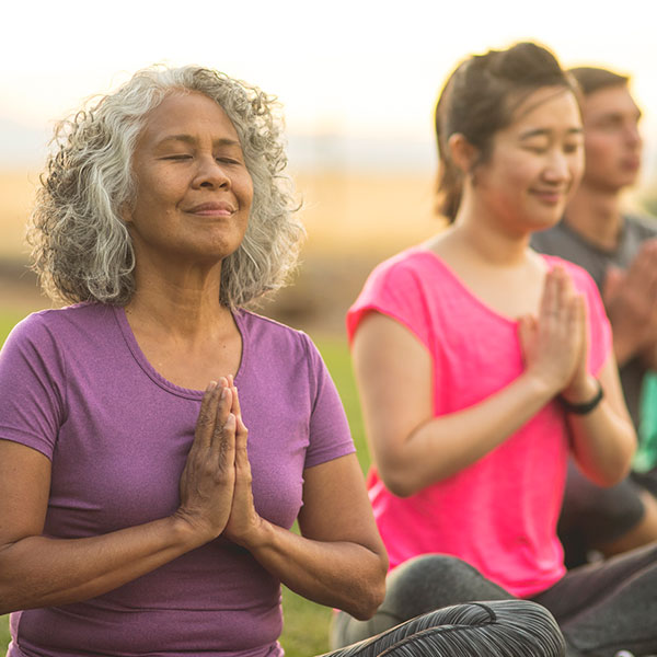 Middle aged women and men outside doing yoga in an open field.