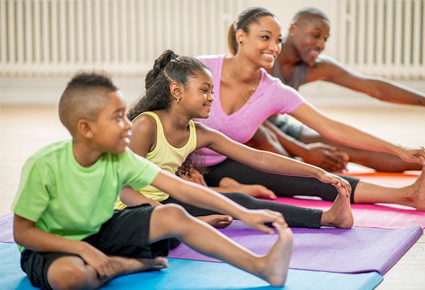 Young african-american family with husband, wife, son and daughter doing yoga together