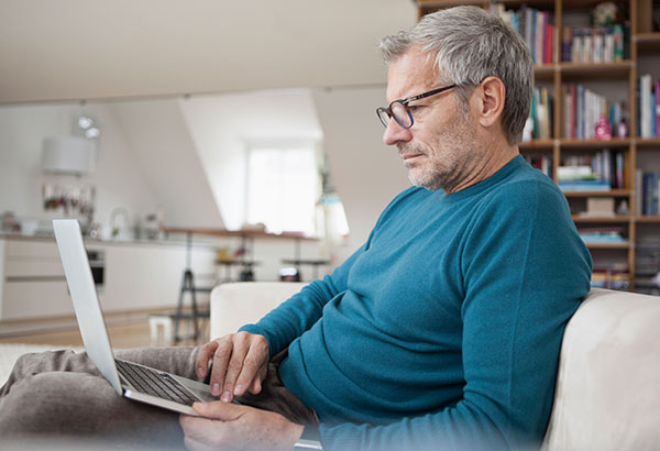 Mature man at home sitting on couch using laptop