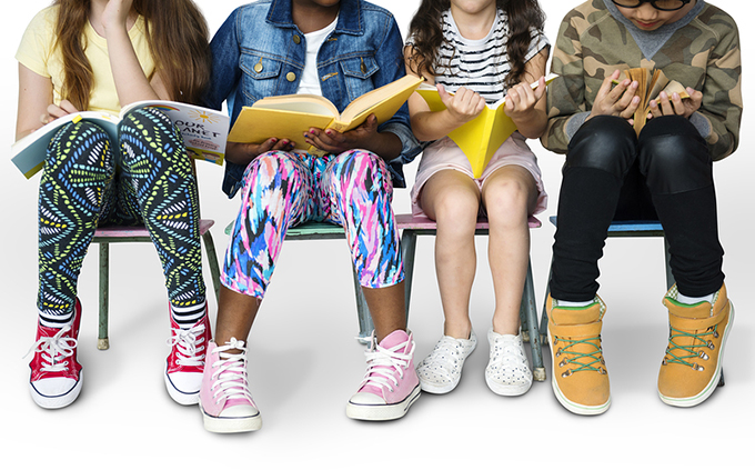 Close up photo of the feet of 4 young children all wearing different colored shoes.