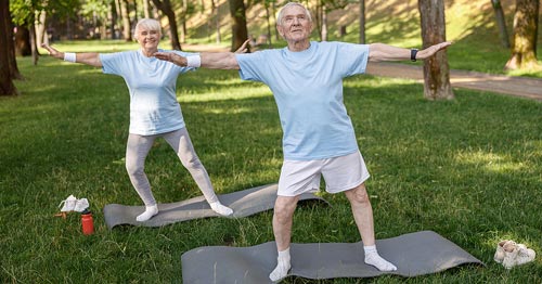 Two senior people doing yoga in a park.