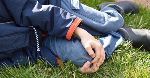 A child lying on the grass grabbing the knee.