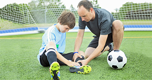 An injured youth soccer player's lower leg being examined by an athletic trainer.