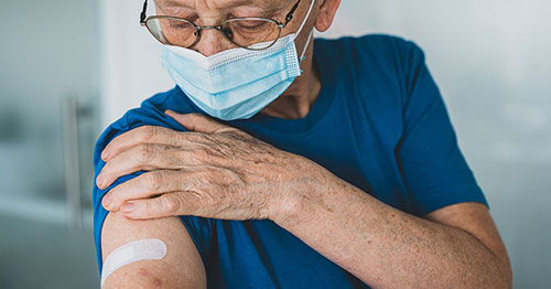 An older person holding their sleeve up after vaccination.