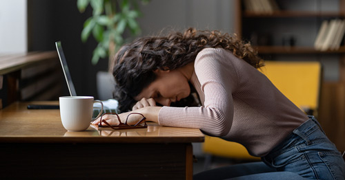 A fatigued woman slumped over her desk.