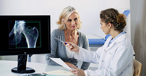 A doctor and patient talking in front of an X-ray of the patient's hip arthritis.