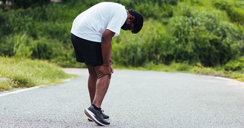 A male jogger grabbing his outer knee in pain.