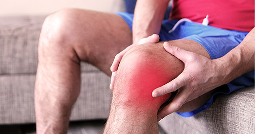 A man grasping his knee, which is red from warmth or swelling.