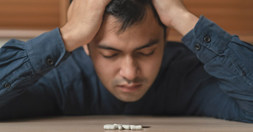 A man with pain looking depressed with pills on a table.