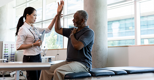 A physical therapist wroking with a patient raising their arm.