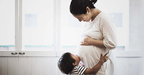 A pregnant woman smiling at her toddler.