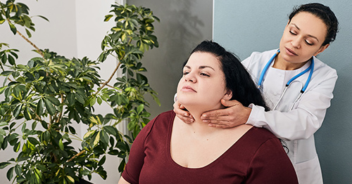 A female doctor conducting a physical examination of a female patient's thyroid.